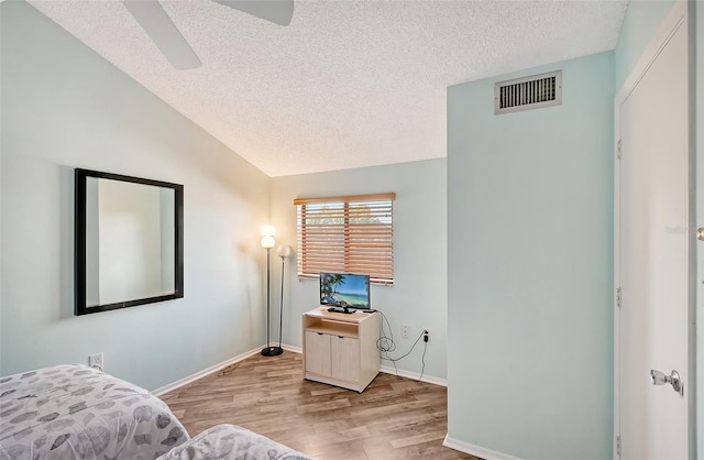 bedroom featuring ceiling fan, vaulted ceiling, a textured ceiling, and light hardwood / wood-style flooring