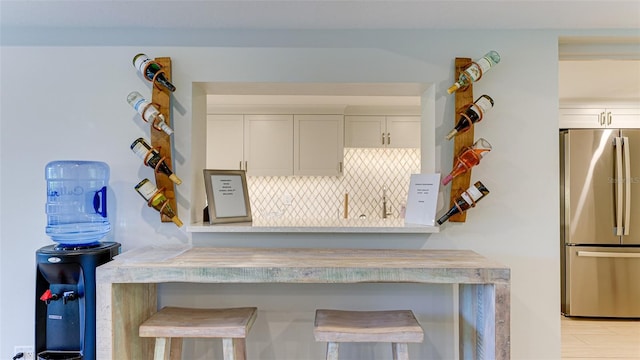 kitchen with tasteful backsplash, a kitchen bar, stainless steel refrigerator, white cabinetry, and light wood-type flooring