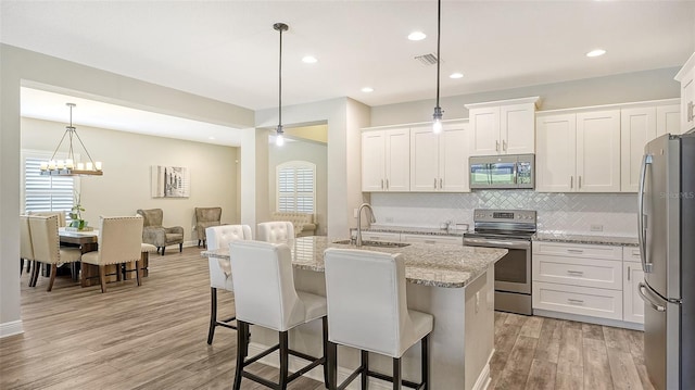 kitchen featuring light hardwood / wood-style floors, white cabinetry, hanging light fixtures, a kitchen breakfast bar, and stainless steel appliances