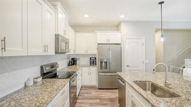 kitchen with sink, white cabinets, light hardwood / wood-style flooring, appliances with stainless steel finishes, and decorative light fixtures