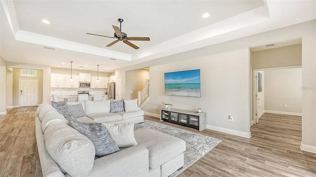 living room featuring light hardwood / wood-style floors, a tray ceiling, and ceiling fan