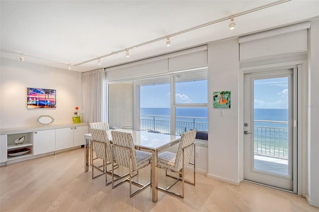 dining area featuring track lighting, light wood-style floors, and a water view