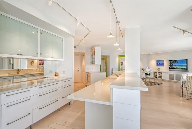 kitchen with light wood finished floors, stovetop, light countertops, rail lighting, and modern cabinets