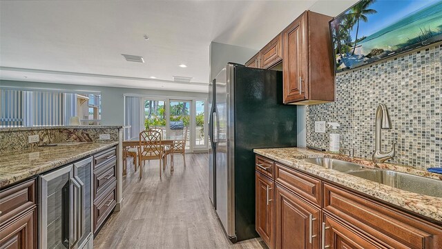 kitchen with light stone counters, freestanding refrigerator, a sink, tasteful backsplash, and light wood-type flooring