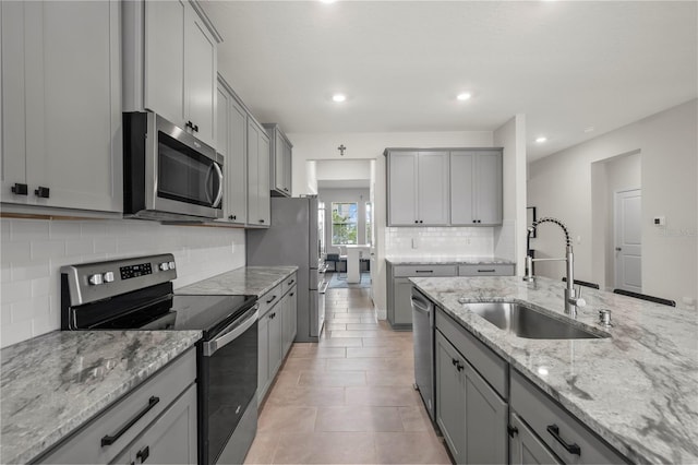 kitchen featuring gray cabinetry, light stone countertops, backsplash, appliances with stainless steel finishes, and sink