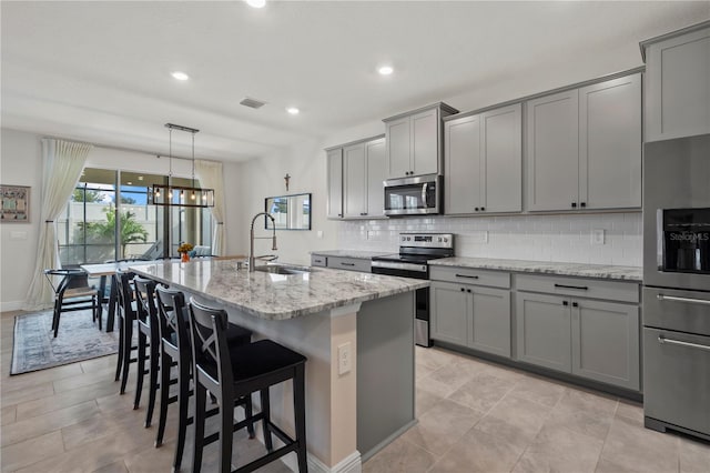 kitchen featuring appliances with stainless steel finishes, light stone countertops, sink, a kitchen island with sink, and a breakfast bar