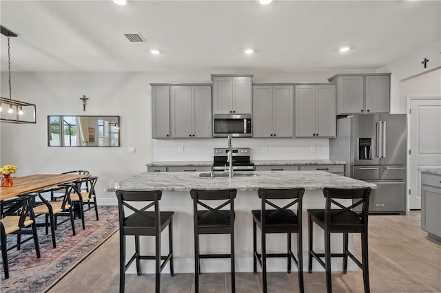 kitchen featuring decorative light fixtures, light stone countertops, a center island with sink, tasteful backsplash, and stainless steel appliances