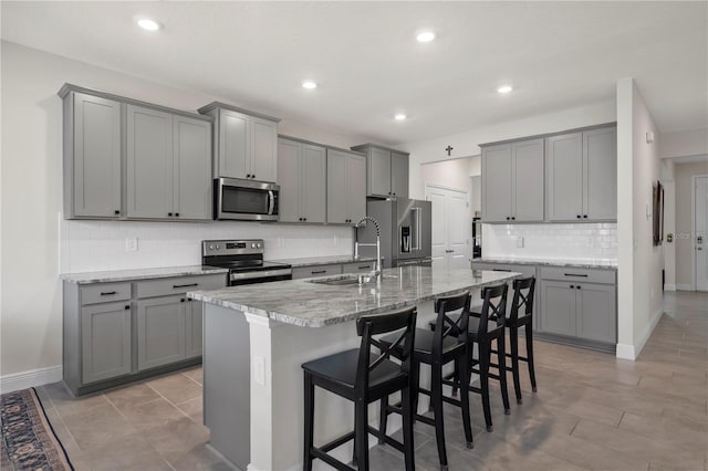 kitchen featuring gray cabinets, sink, a breakfast bar, appliances with stainless steel finishes, and a center island with sink