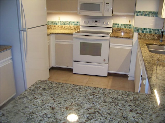 kitchen with light tile patterned floors, backsplash, light stone countertops, and white appliances