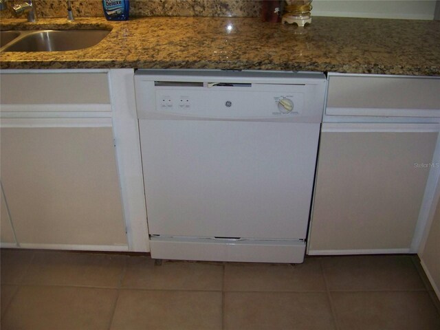 room details with tile patterned flooring, white dishwasher, dark stone counters, and sink