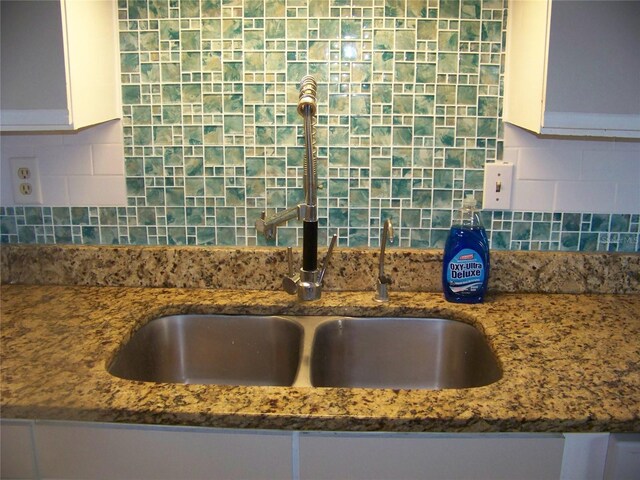 details with dark stone counters, sink, white cabinetry, and tasteful backsplash