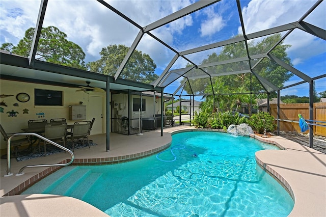 view of pool with glass enclosure, pool water feature, ceiling fan, and a patio area