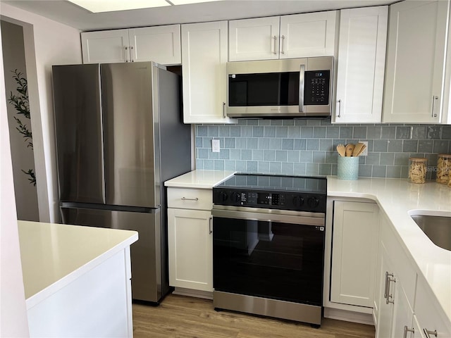 kitchen featuring light wood-type flooring, backsplash, stainless steel appliances, and white cabinetry