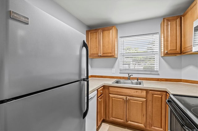 kitchen featuring white dishwasher, range with electric stovetop, stainless steel refrigerator, and sink