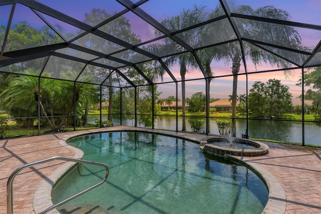 pool at dusk featuring a lanai, an in ground hot tub, and a water view