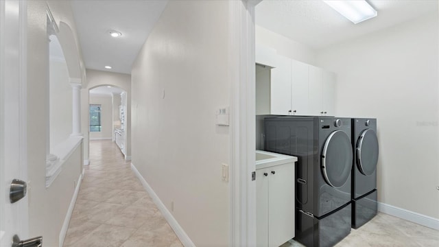 clothes washing area with decorative columns, independent washer and dryer, light tile patterned floors, and cabinets