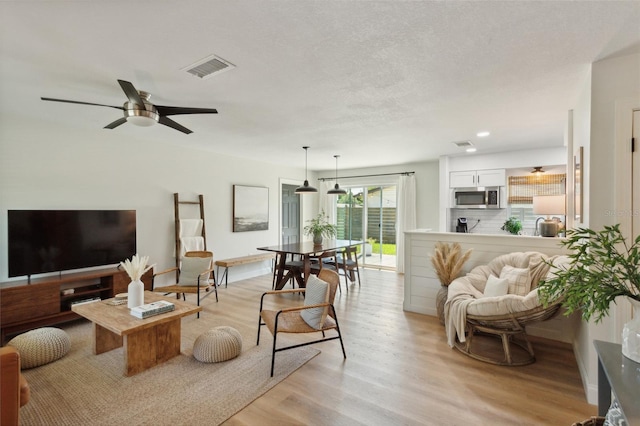 living room featuring a textured ceiling, light wood-type flooring, and ceiling fan