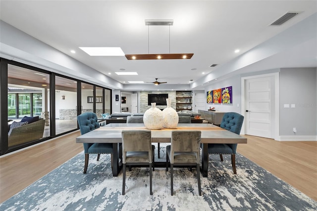 dining area with ceiling fan, a skylight, and light wood-type flooring