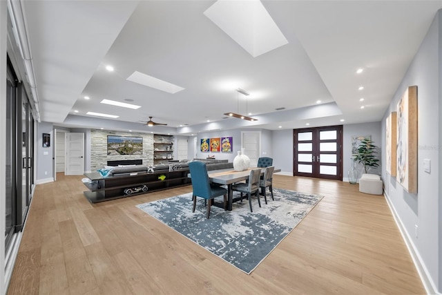 dining area with a raised ceiling, ceiling fan, light hardwood / wood-style flooring, and a skylight