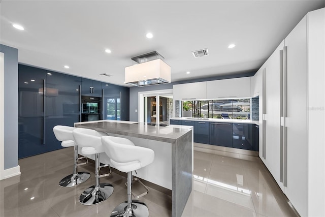 kitchen featuring a kitchen breakfast bar, white cabinetry, a kitchen island, blue cabinetry, and light tile patterned floors