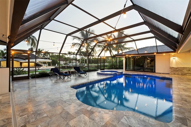 pool at dusk with a patio, glass enclosure, and an in ground hot tub