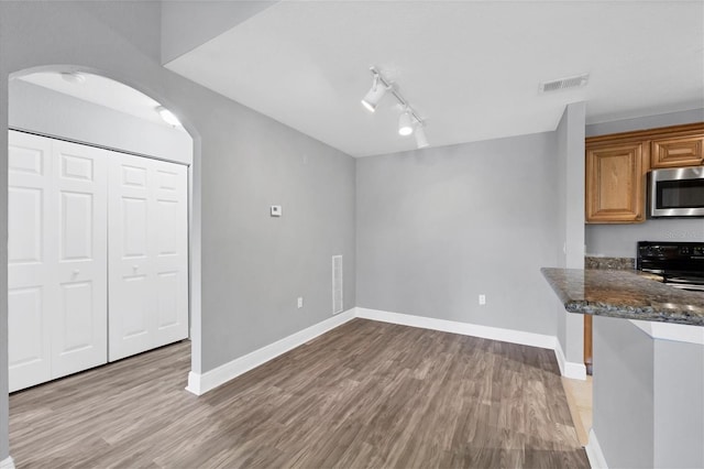 kitchen with black stove, rail lighting, dark stone countertops, and light hardwood / wood-style floors