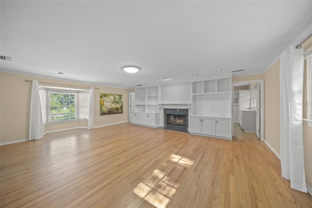 unfurnished living room featuring light hardwood / wood-style flooring, built in features, a fireplace, and crown molding