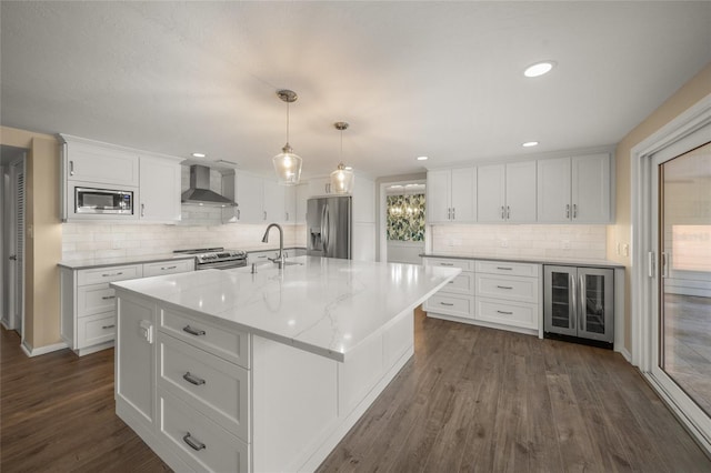 kitchen with white cabinets, wine cooler, a center island with sink, wall chimney range hood, and stainless steel appliances