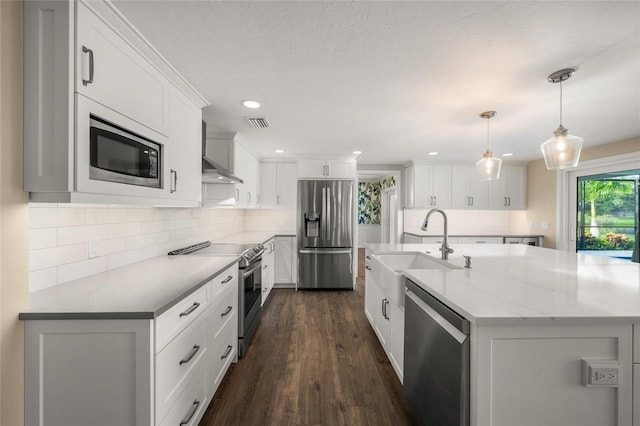 kitchen with appliances with stainless steel finishes, white cabinets, pendant lighting, sink, and wall chimney range hood