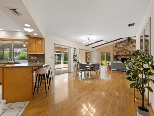 interior space featuring dark stone counters, vaulted ceiling with beams, backsplash, kitchen peninsula, and a breakfast bar