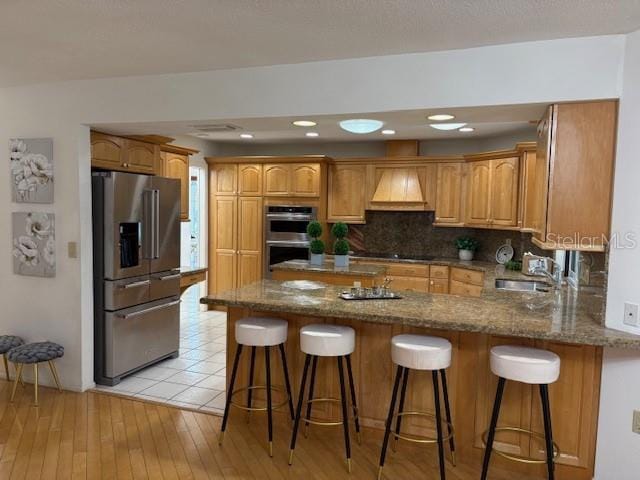 kitchen with a kitchen breakfast bar, appliances with stainless steel finishes, sink, custom exhaust hood, and backsplash