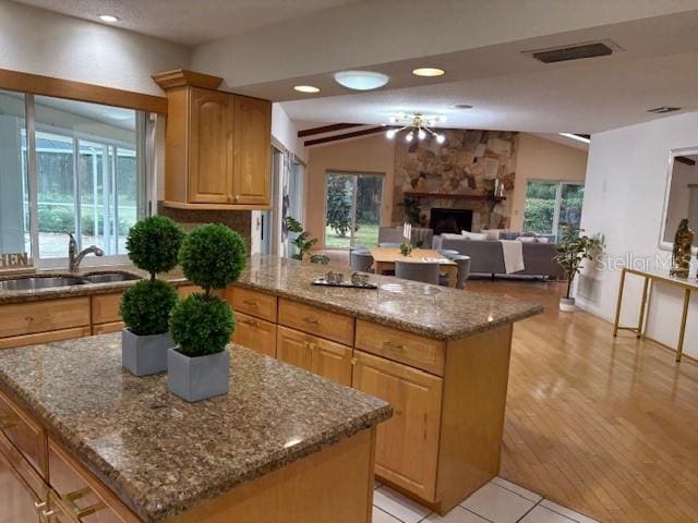 kitchen featuring light stone countertops, a center island, a fireplace, sink, and vaulted ceiling