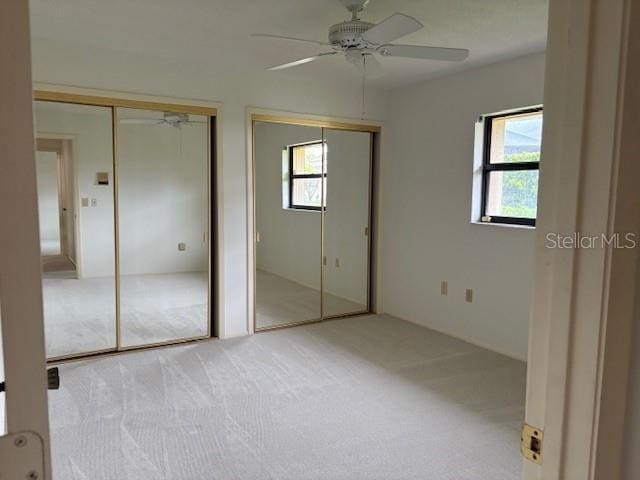 unfurnished bedroom featuring multiple closets, light colored carpet, and ceiling fan