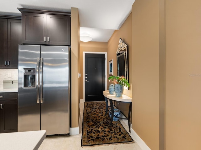 kitchen with light tile patterned floors, stainless steel fridge, decorative backsplash, and dark brown cabinets