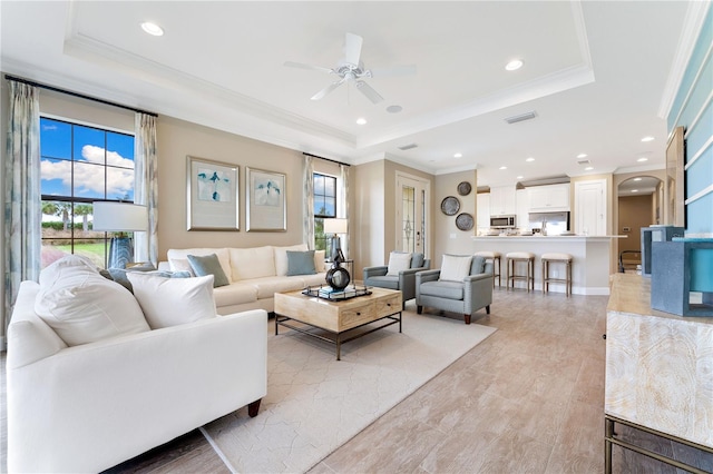 living room with a raised ceiling, ceiling fan, and a healthy amount of sunlight