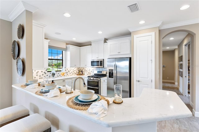 kitchen featuring white cabinets, stainless steel appliances, a kitchen breakfast bar, decorative backsplash, and ornamental molding