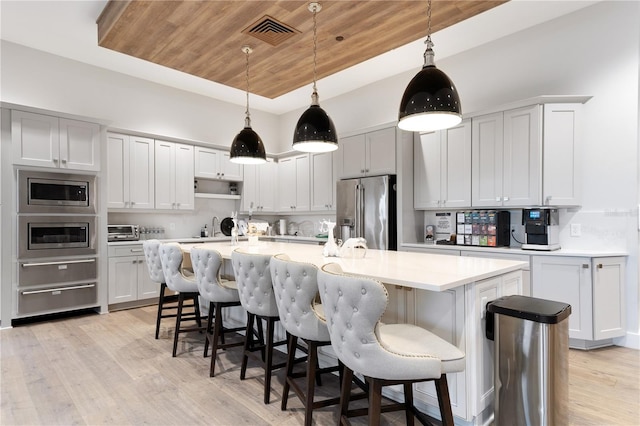 kitchen featuring a breakfast bar area, light hardwood / wood-style floors, wood ceiling, a kitchen island with sink, and stainless steel appliances