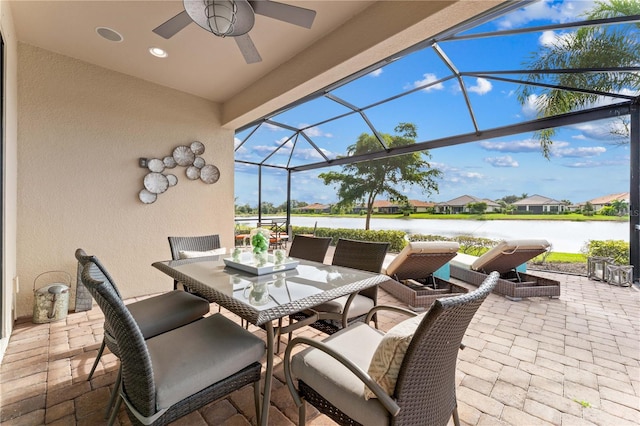 view of patio with a water view, ceiling fan, and glass enclosure