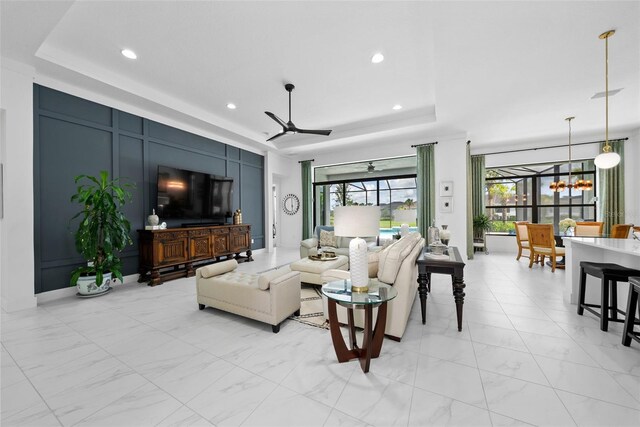 living room featuring ceiling fan with notable chandelier and a tray ceiling