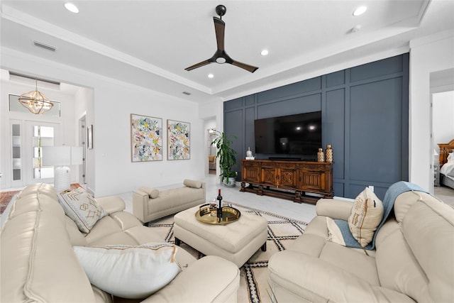 carpeted living room with ceiling fan with notable chandelier, ornamental molding, and a raised ceiling