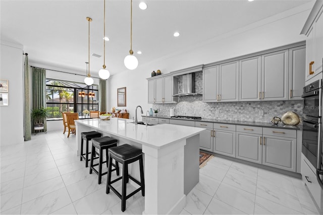 kitchen with a center island with sink, wall chimney range hood, and gray cabinets