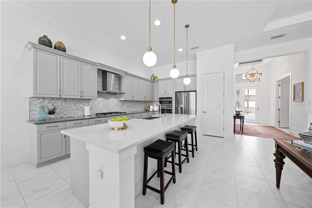 kitchen with an island with sink, wall chimney exhaust hood, pendant lighting, and stainless steel appliances