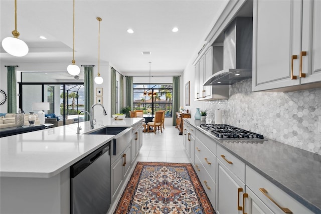 kitchen with a healthy amount of sunlight, stainless steel appliances, a center island with sink, and wall chimney range hood