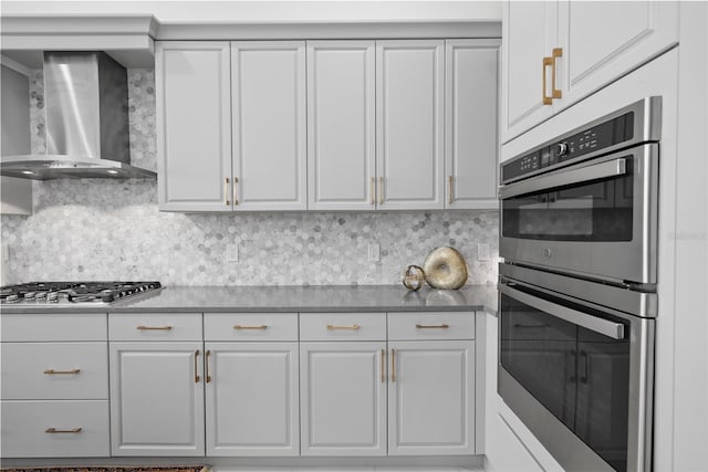 kitchen featuring wall chimney exhaust hood, stainless steel appliances, white cabinets, and decorative backsplash