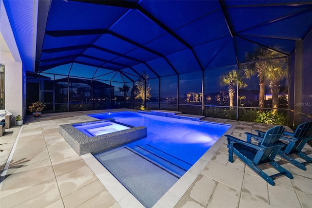 pool at twilight with an in ground hot tub, glass enclosure, and a patio area