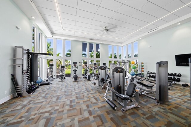 exercise room with carpet floors, a towering ceiling, and ceiling fan