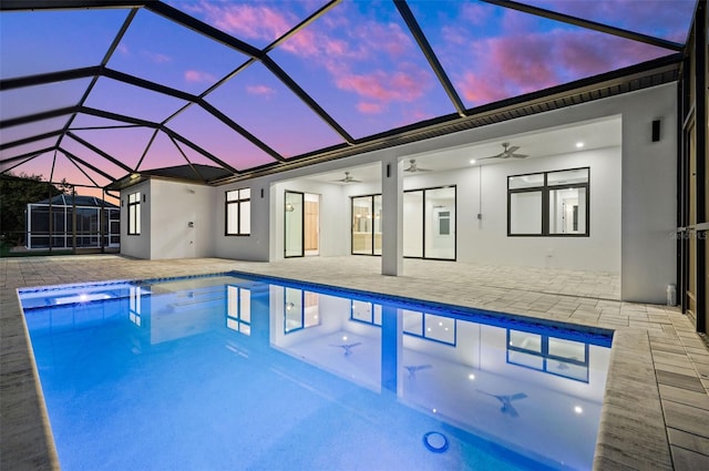 pool at dusk featuring glass enclosure, a patio area, and ceiling fan