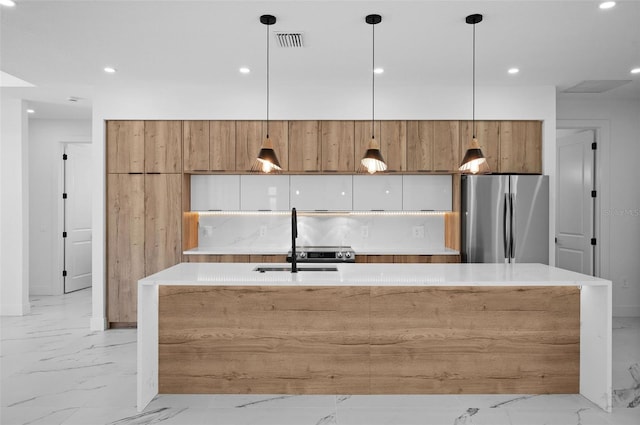 kitchen with sink, stainless steel fridge, an island with sink, pendant lighting, and tasteful backsplash