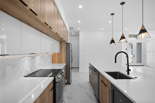 kitchen with hanging light fixtures, appliances with stainless steel finishes, light stone countertops, sink, and decorative backsplash