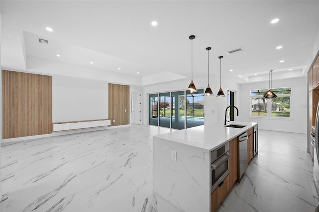 kitchen featuring pendant lighting, wooden walls, sink, an island with sink, and appliances with stainless steel finishes